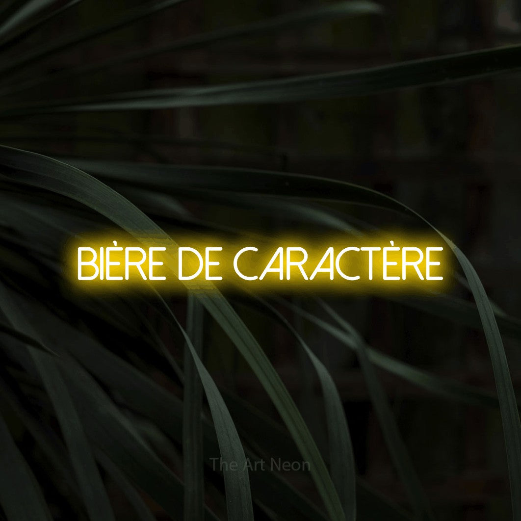 “Bière de caractère” LED neon sign in yellow, with thin sans-serif lettering, shown against a close-up of dark foliage.