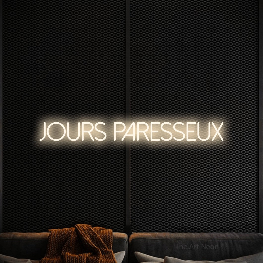 “Jours paresseux” LED neon sign in warm white, with thin sans-serif lettering, shown against a modern dark-toned seating area.