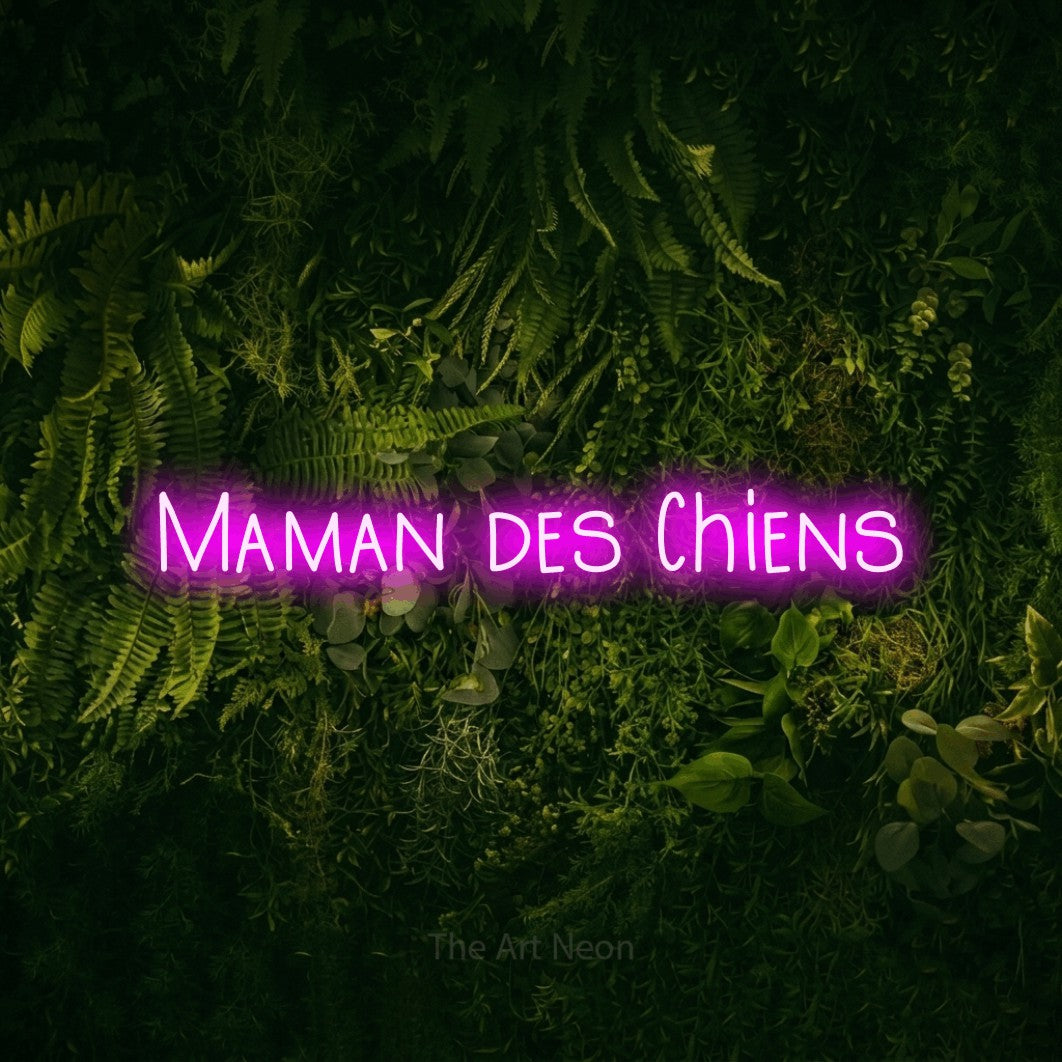 “Maman des chiens” LED neon sign in pink, with narrow hand-drawn lettering, shown against a dark moss and forest backdrop.