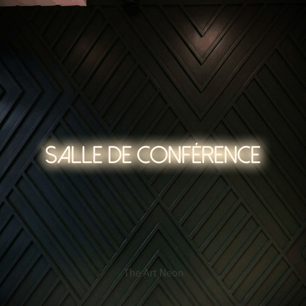 “Salle de conférence” LED neon sign in warm white, with thin sans-serif lettering, shown against a black chevron-patterned wood wall.