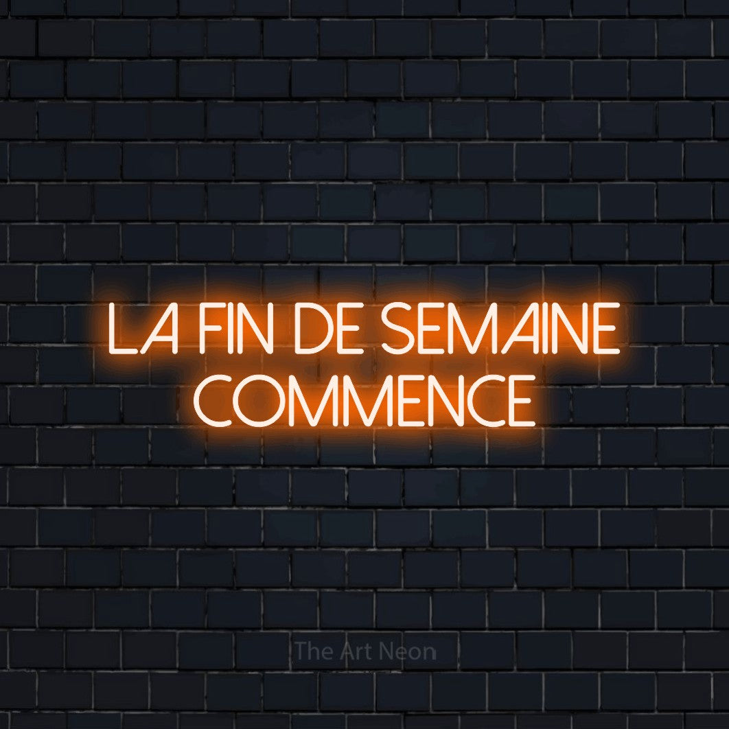 Néon LED « La fin de semaine commence » sur deux lignes en orange, en lettres fines sans empattement, mis en scène sur un mur de briques bleu marine foncé, pour un bar ou un pub.