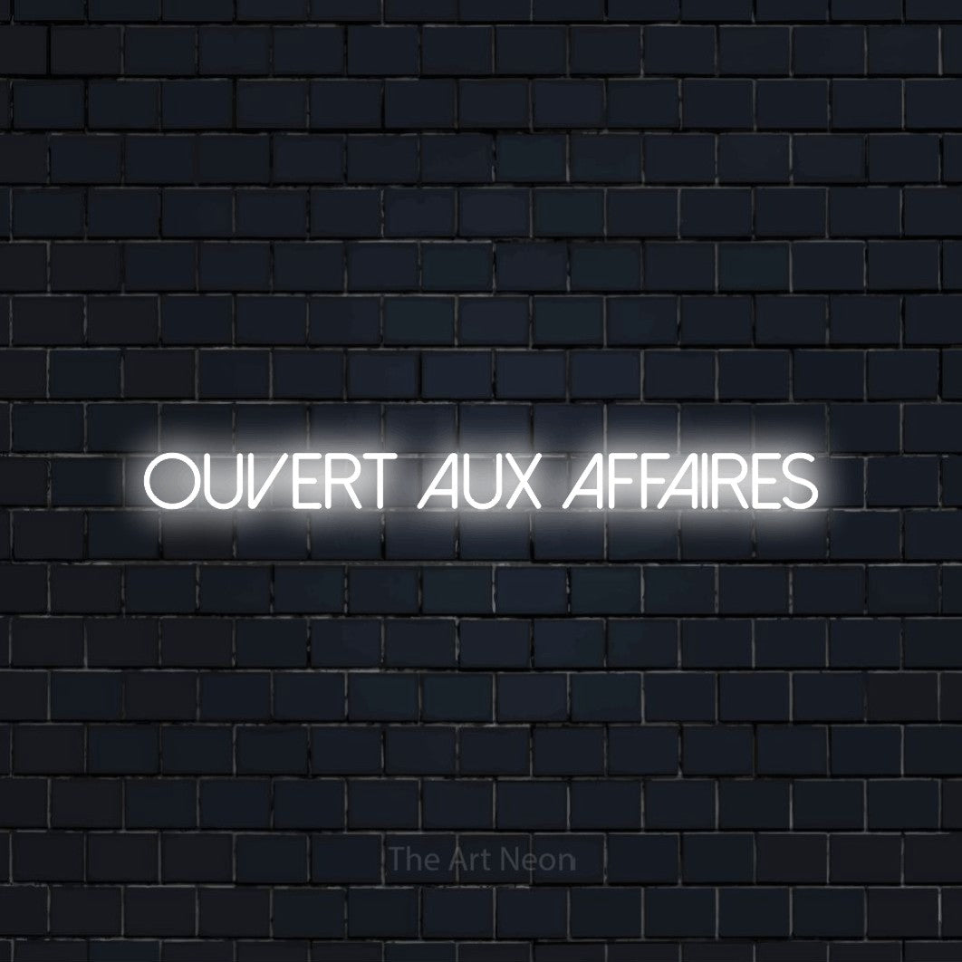 “Ouvert aux affaires” LED neon sign in cool white, with thin sans-serif lettering, shown against a dark navy brick wall.