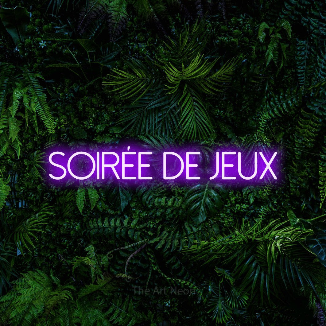 “Soirée de jeux” LED neon sign in purple, with thin sans-serif lettering, shown against dense tropical foliage.