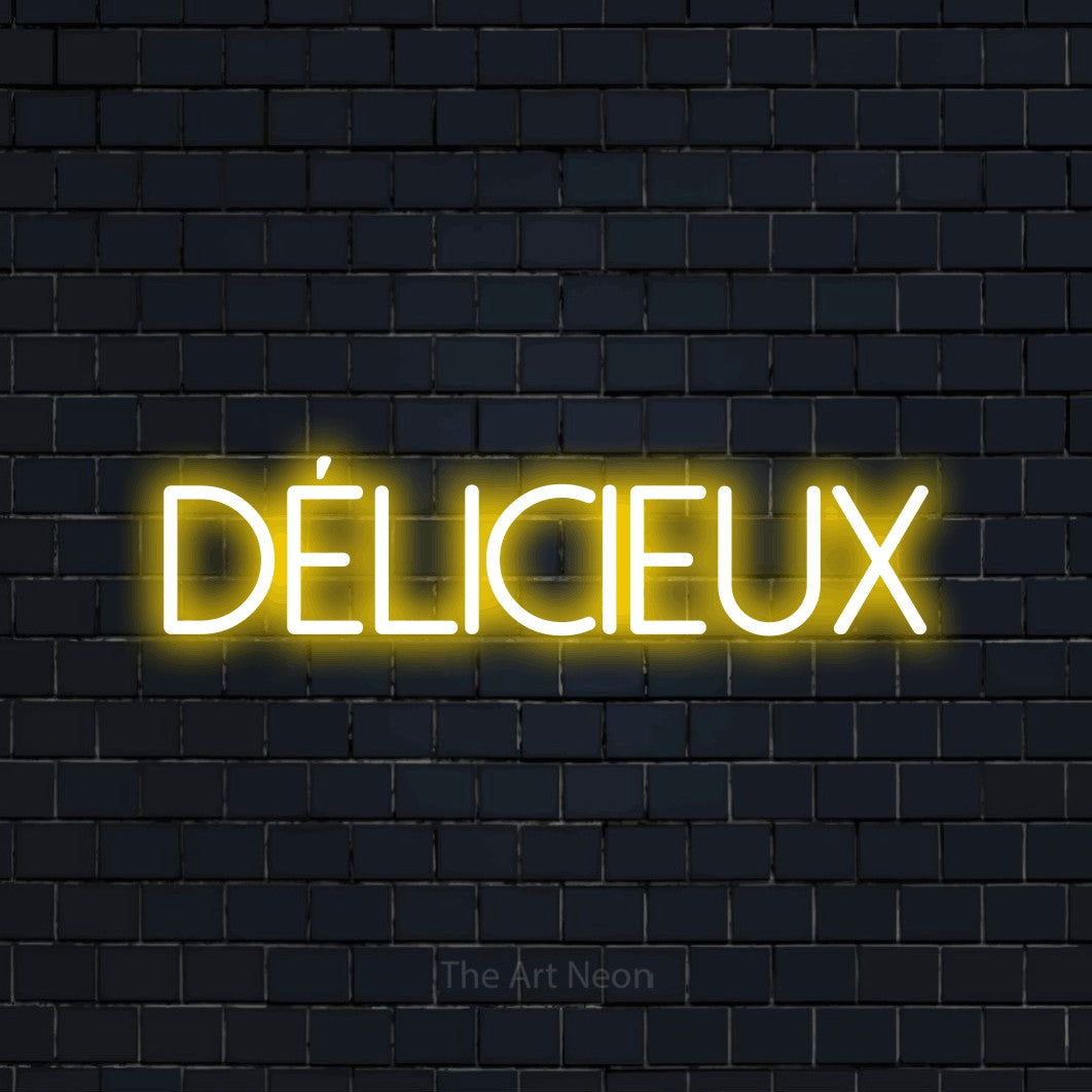 “Délicieux” LED neon sign in yellow, with thin sans-serif lettering, shown against a dark navy brick wall.