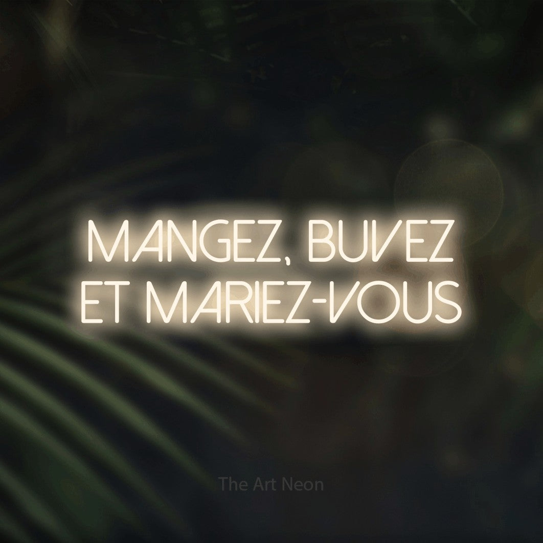 “Mangez, buvez et mariez-vous” LED neon sign in warm white, with thin sans-serif lettering across 2 lines, shown against a blurred palm and bokeh-light backdrop.