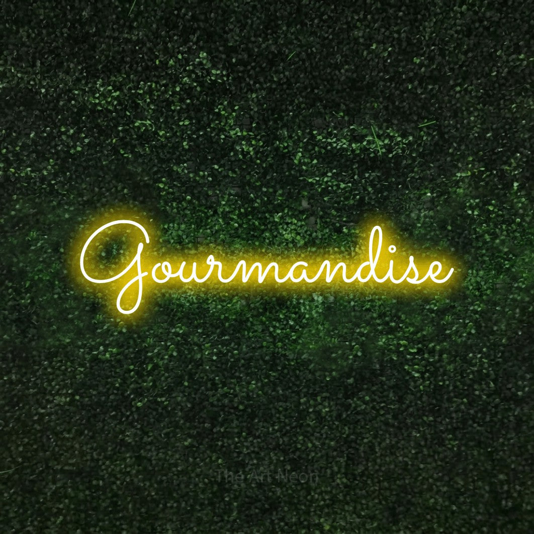 “Gourmandise” LED neon sign in yellow, with looped cursive lettering, shown against a textured green hedge.