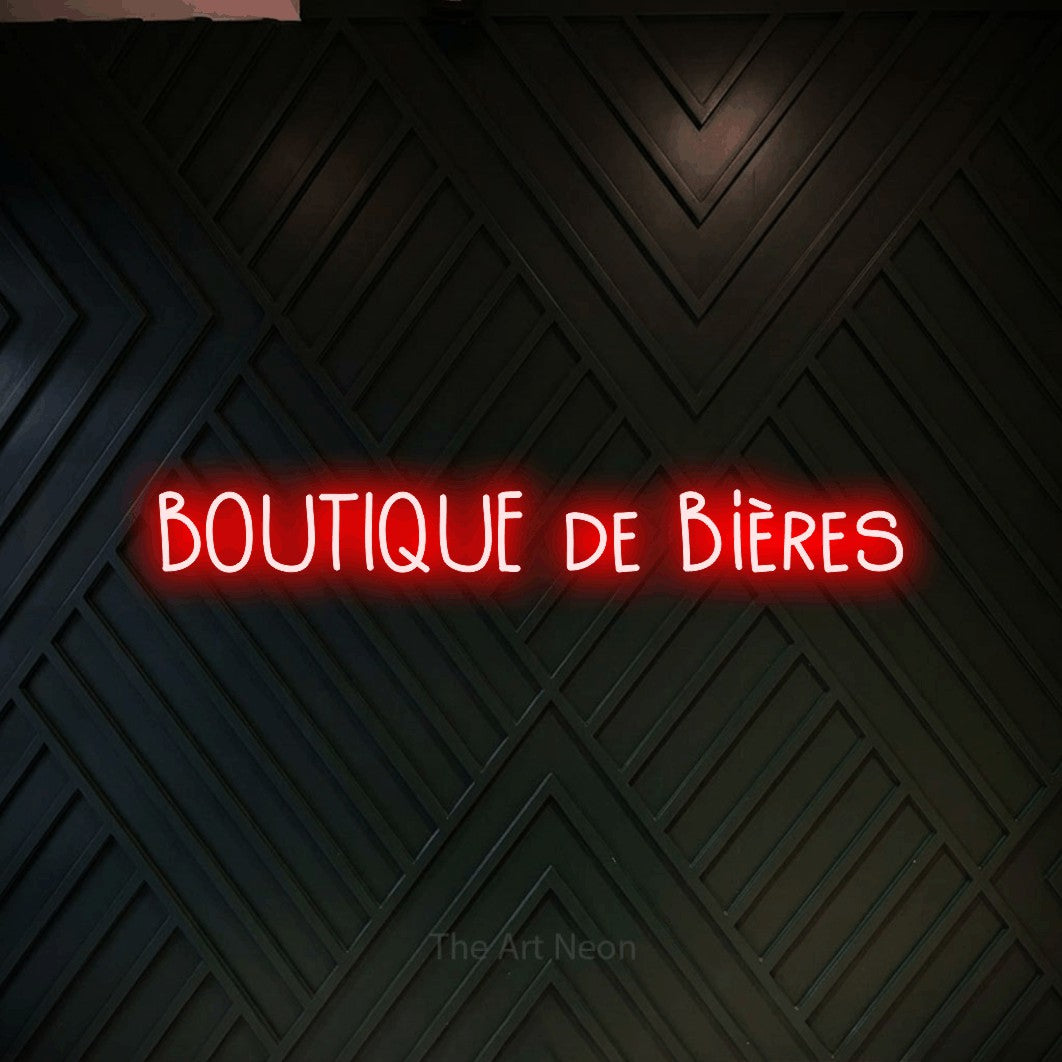 “Boutique de bières” LED neon sign in red, with narrow hand-drawn lettering, shown against a black chevron-patterned wood wall.