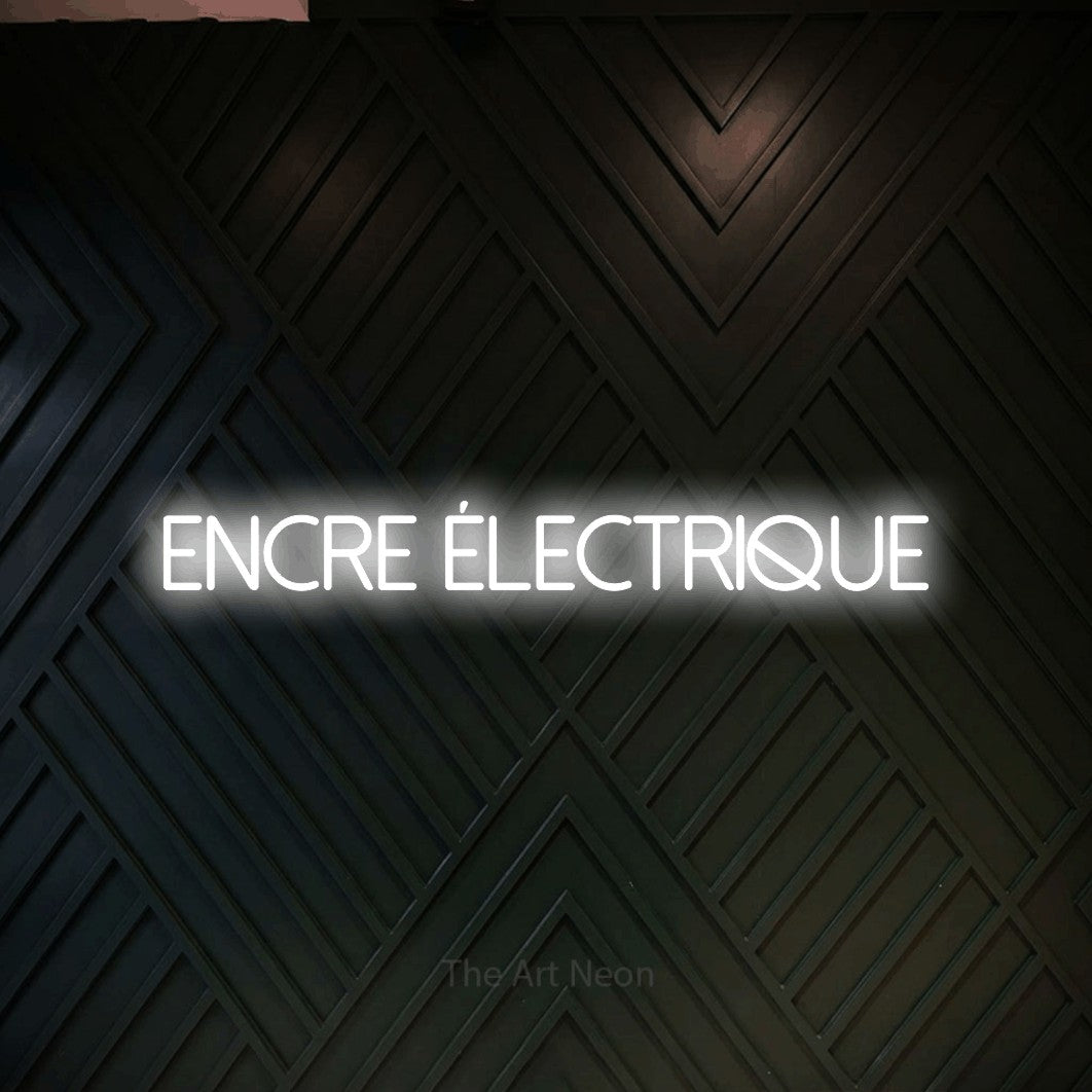 “Encre électrique” LED neon sign in cool white, with thin sans-serif lettering, shown against a black chevron-patterned wood wall.