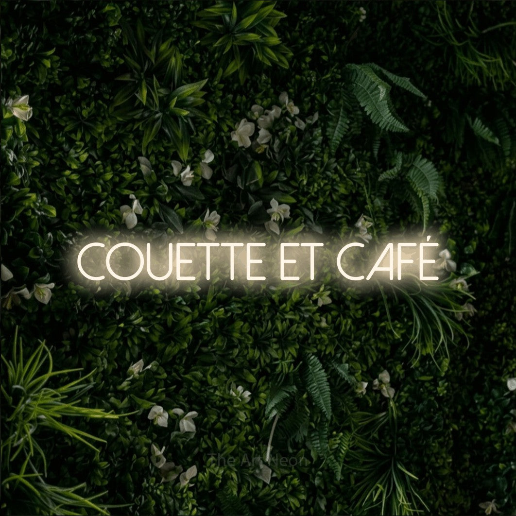 Enseigne néon LED « Couette et café » en blanc chaud, en lettres fines sans empattement, présentée sur un mur végétal vert et dense, pour un hôtel.
