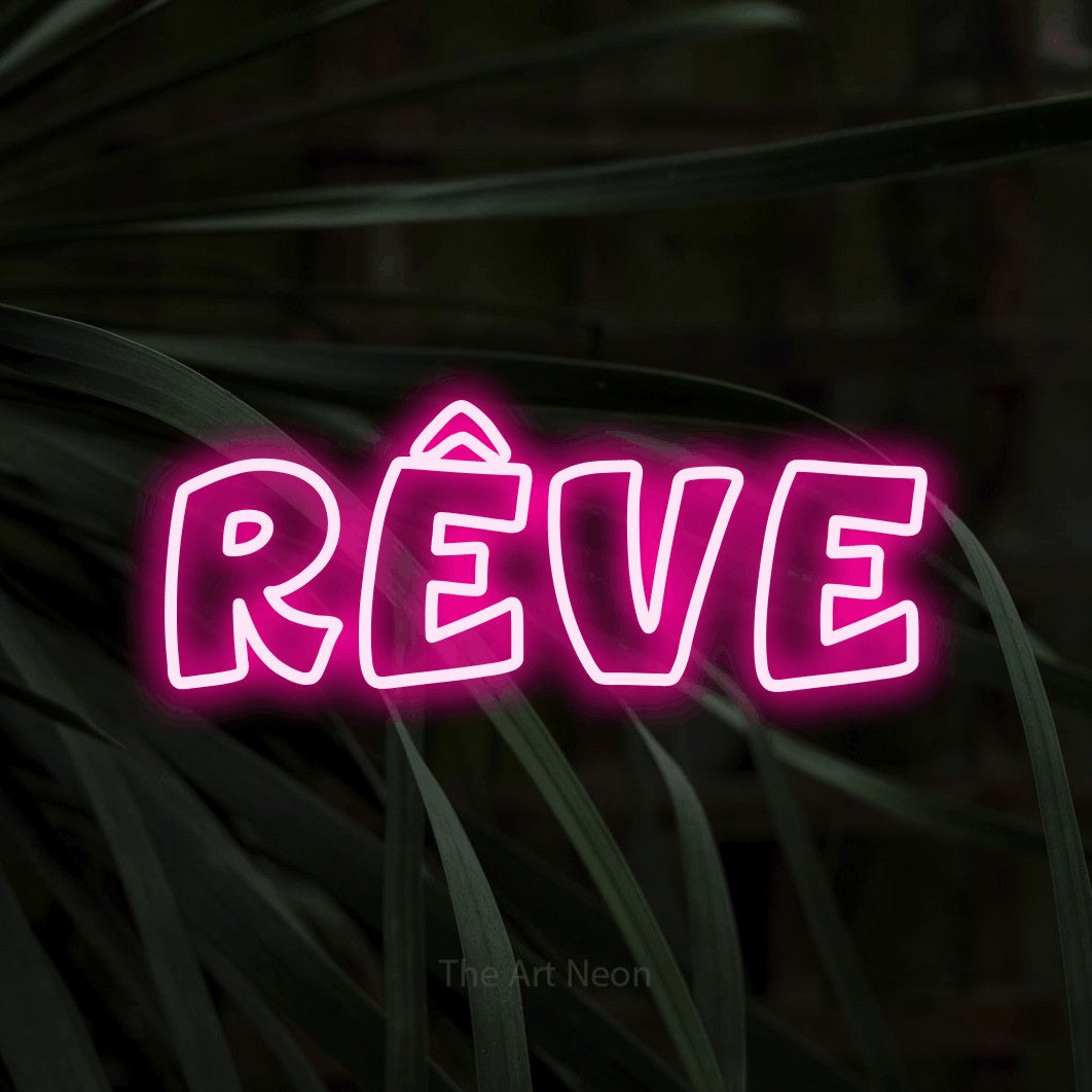 “Rêve” LED neon sign in hot pink, with rounded outline lettering, shown against a close-up of dark foliage.