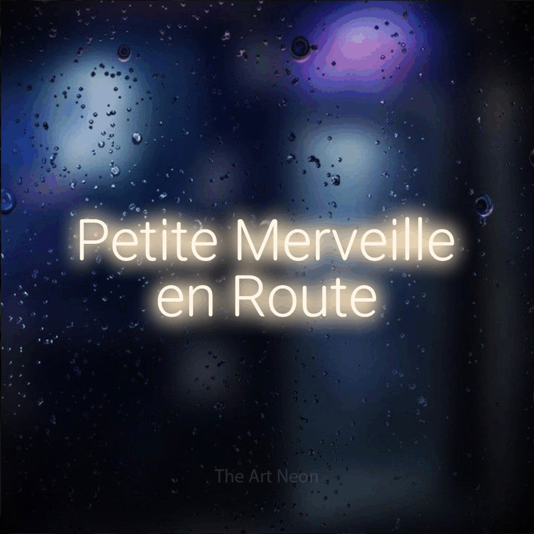 Enseigne néon LED « Petite merveille en route » sur deux lignes en blanc chaud, en lettres sans empattement arrondies, présentée sur une vitre aux reflets bleus et violets, pour une fête prénatale.