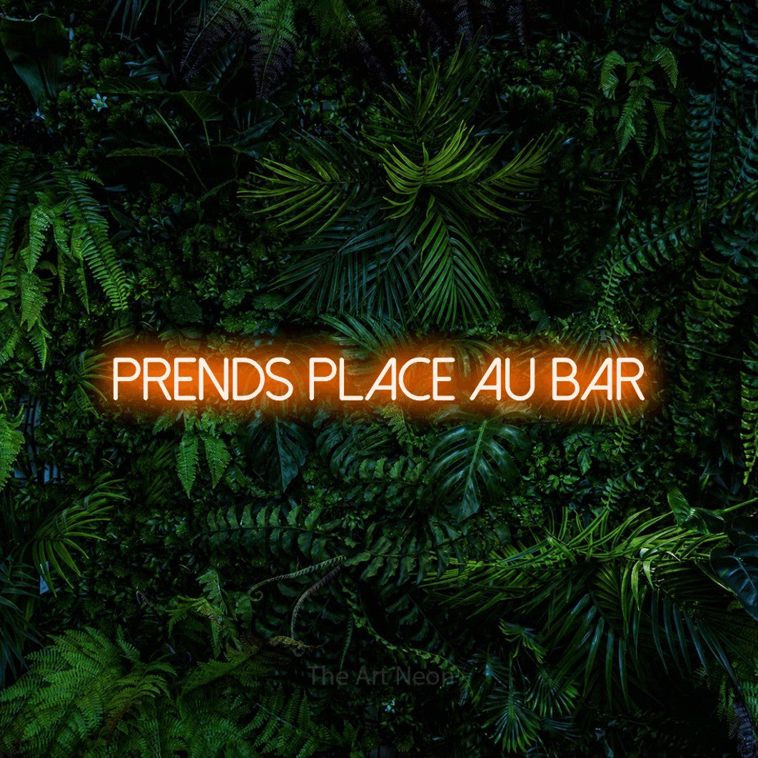 “Prends place au bar” LED neon sign in orange, with thin sans-serif lettering, shown against dense tropical foliage.