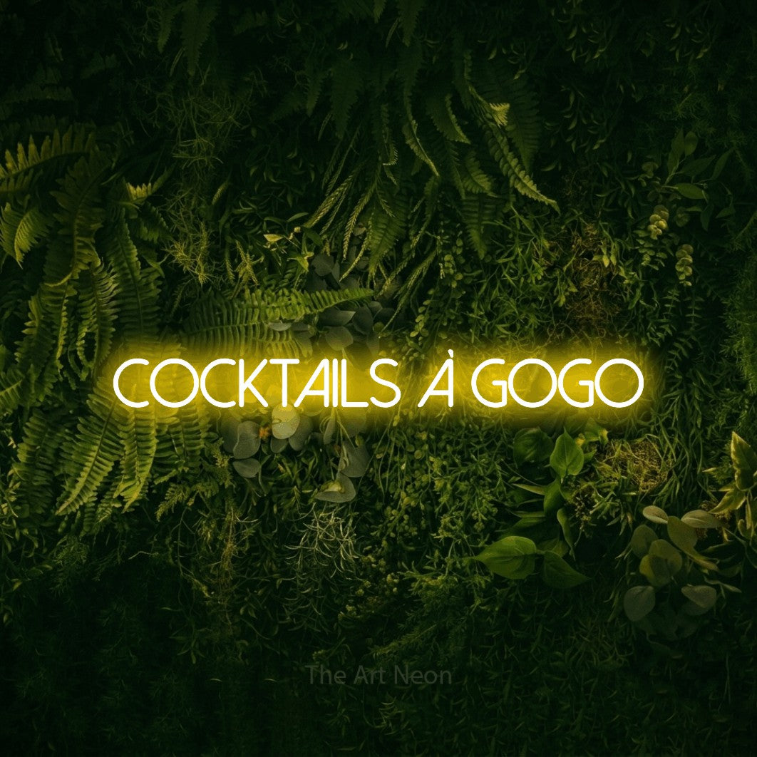 “Cocktails à gogo” LED neon sign in yellow, with thin sans-serif lettering, shown against a dark moss and forest backdrop.