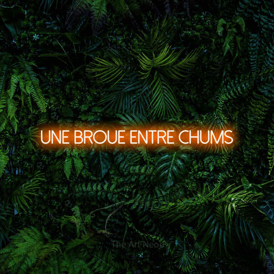 “Une broue entre chums” LED neon sign in orange, with thin sans-serif lettering, shown against dense tropical foliage.