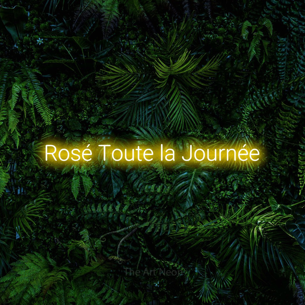 Composition en néon LED « Rosé toute la journée » en jaune, en lettres sans empattement arrondies, mise en valeur devant un feuillage tropical dense, pour une cuisine.