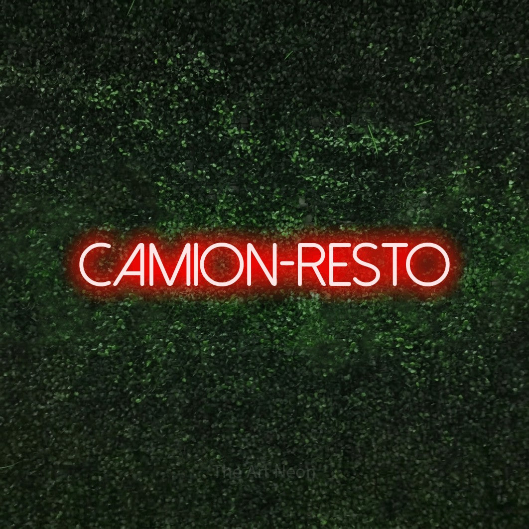 “Camion-resto” LED neon sign in red, with thin sans-serif lettering, shown against a textured green hedge.