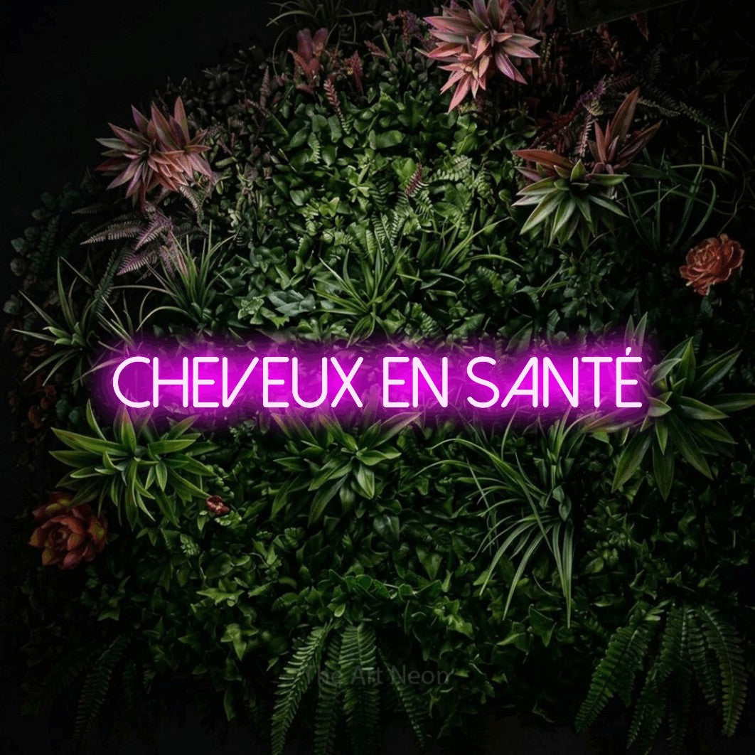 “Cheveux en santé” LED neon sign in pink, with thin sans-serif lettering, shown against a flowering plant wall.