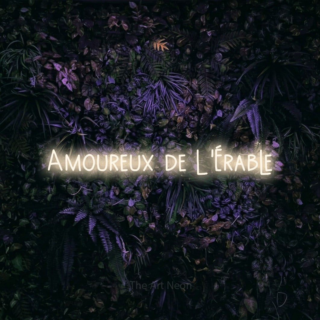 “Amoureux de l'érable” LED neon sign in warm white, with narrow hand-drawn lettering, shown against a dark wall with purple flowers.
