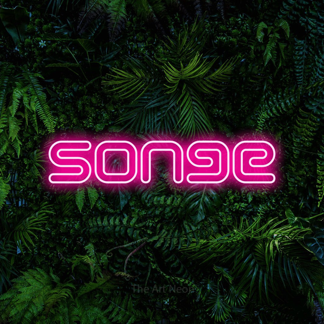 “Songe” LED neon sign in hot pink, with futuristic double-line lettering, shown against dense tropical foliage.