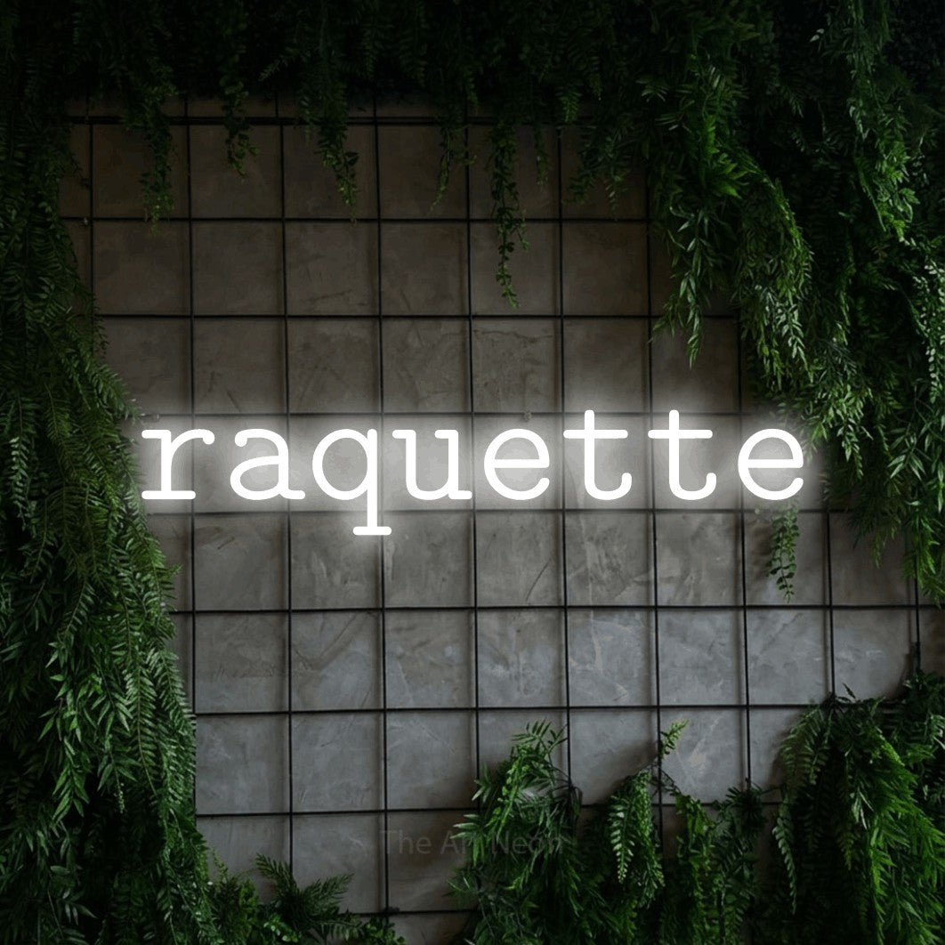 “Raquette” LED neon sign in cool white, with typewriter-style lettering, shown against an ivy-covered concrete grid.