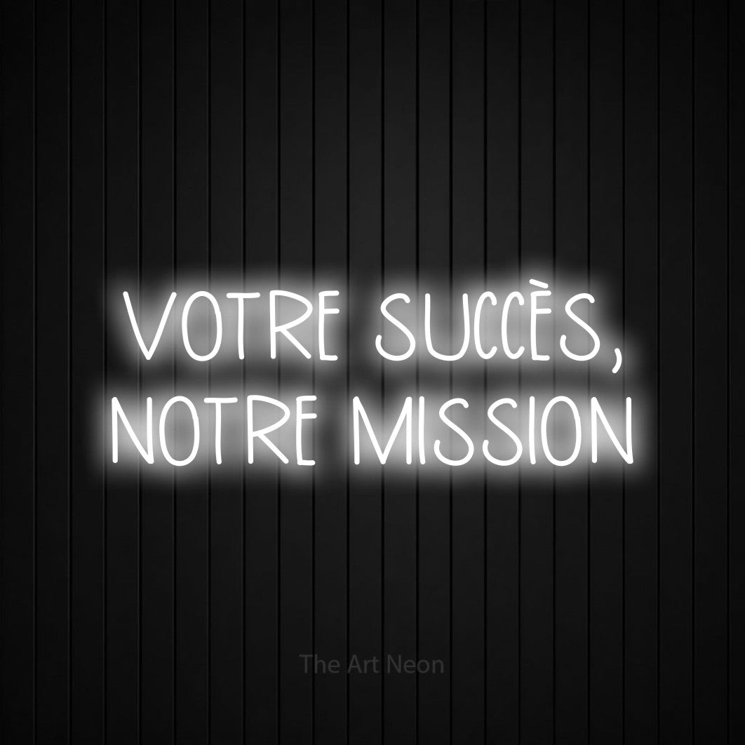 “Votre succès, notre mission” LED neon sign in cool white, with narrow hand-drawn lettering across 2 lines, shown against black vertical wall slats.