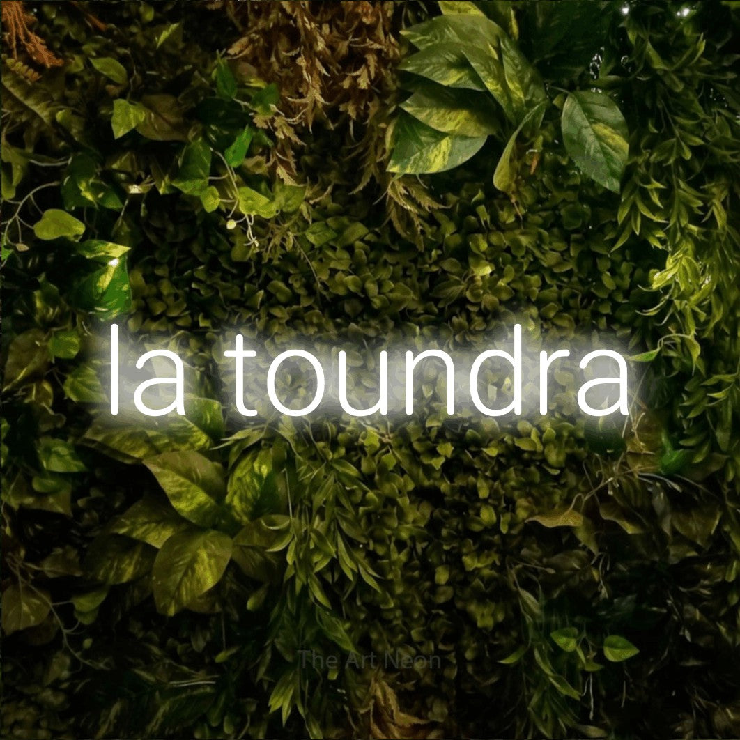 “La toundra” LED neon sign in cool white, with rounded sans-serif lettering, shown against bright green and yellow foliage.
