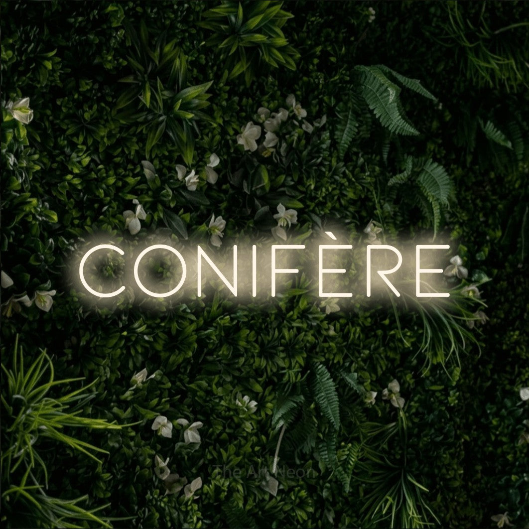 “Conifère” LED neon sign in warm white, with thin, widely spaced lettering, shown against a dense green plant wall.