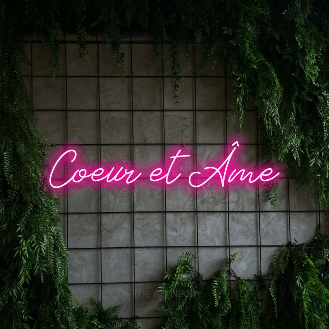 “Cœur et âme” LED neon sign in hot pink, with cursive lettering, shown against an ivy-covered concrete grid.