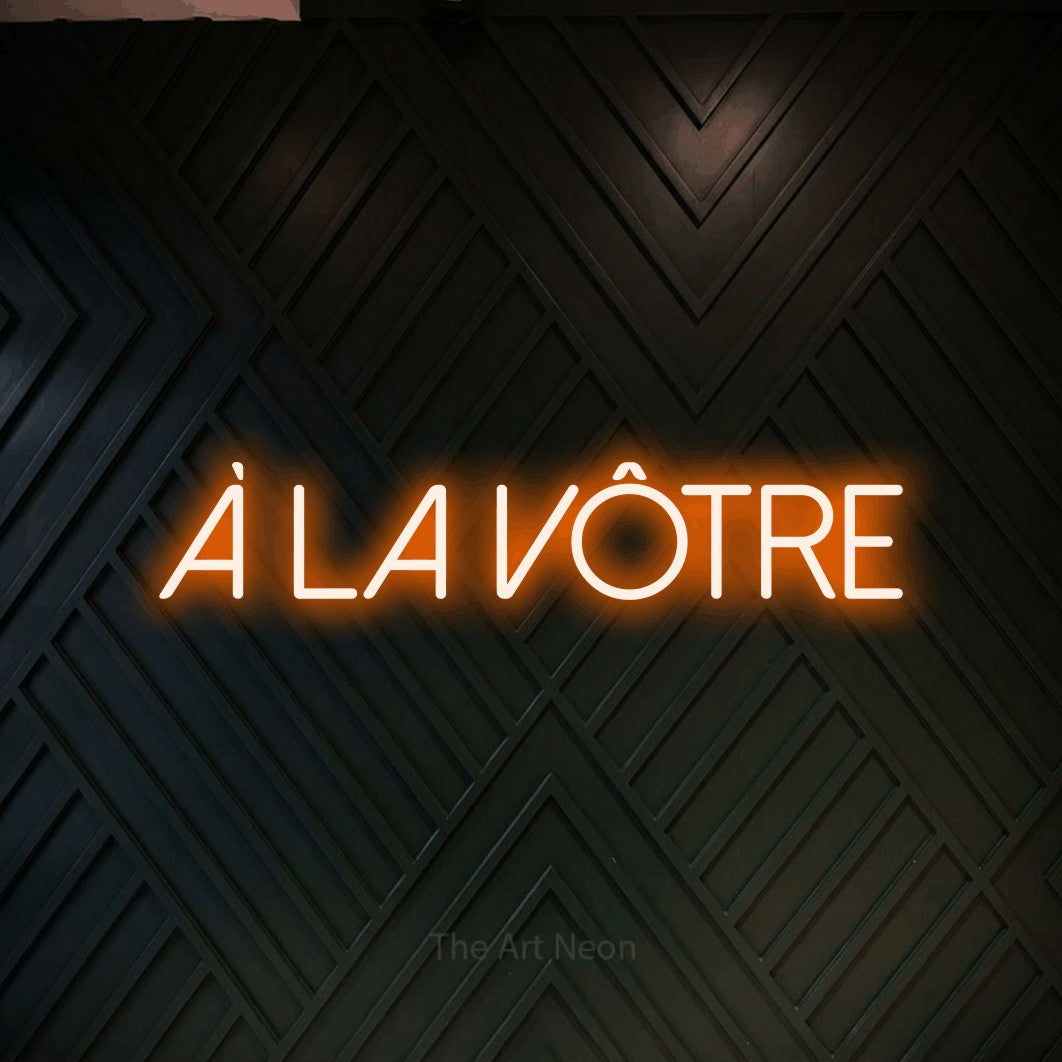 “À la vôtre” LED neon sign in orange, with thin sans-serif lettering, shown against a black chevron-patterned wood wall.