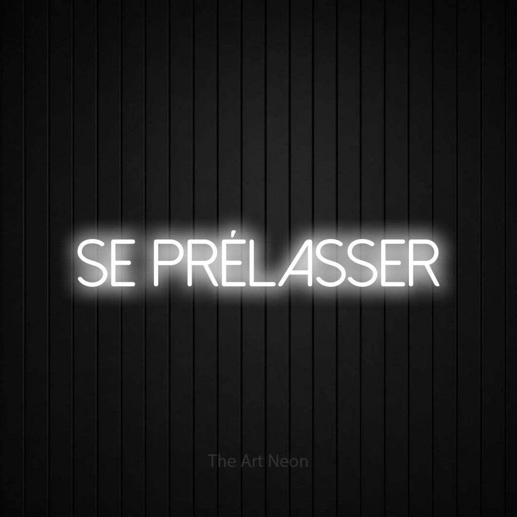 Néon LED « Se prélasser » en blanc froid, en lettres fines sans empattement, mis en scène sur un mur de lattes verticales noires, pour un salon.