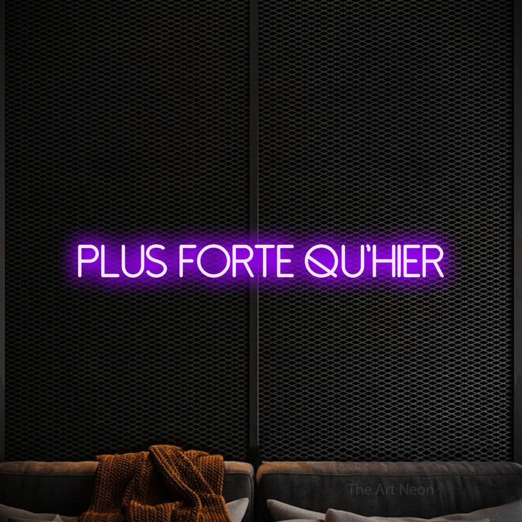 “Plus forte qu'hier” LED neon sign in purple, with thin sans-serif lettering, shown against a modern dark-toned seating area.
