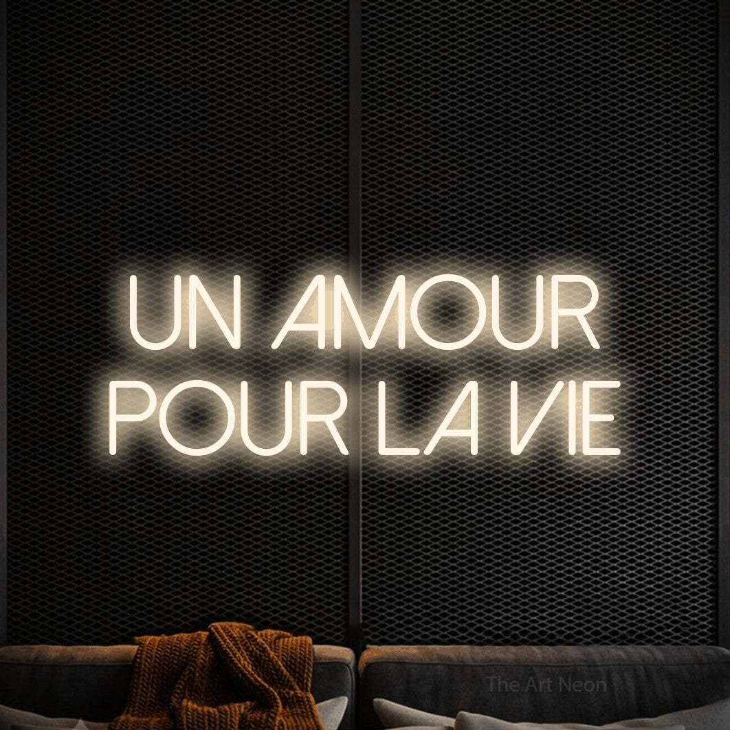 “Un amour pour la vie” LED neon sign in warm white, with thin sans-serif lettering across 2 lines, shown against a modern dark-toned seating area.