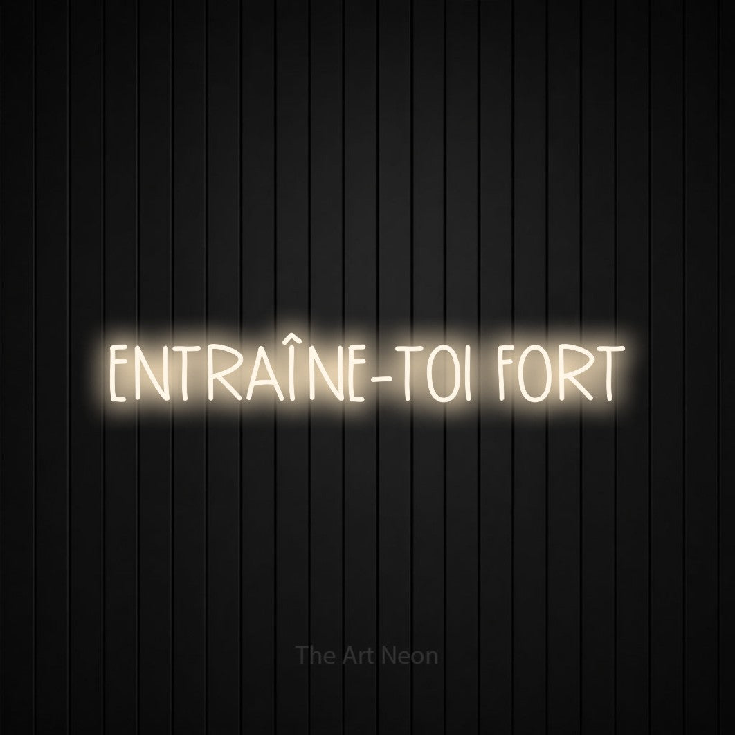 “Entraîne-toi fort” LED neon sign in warm white, with narrow hand-drawn lettering, shown against black vertical wall slats.