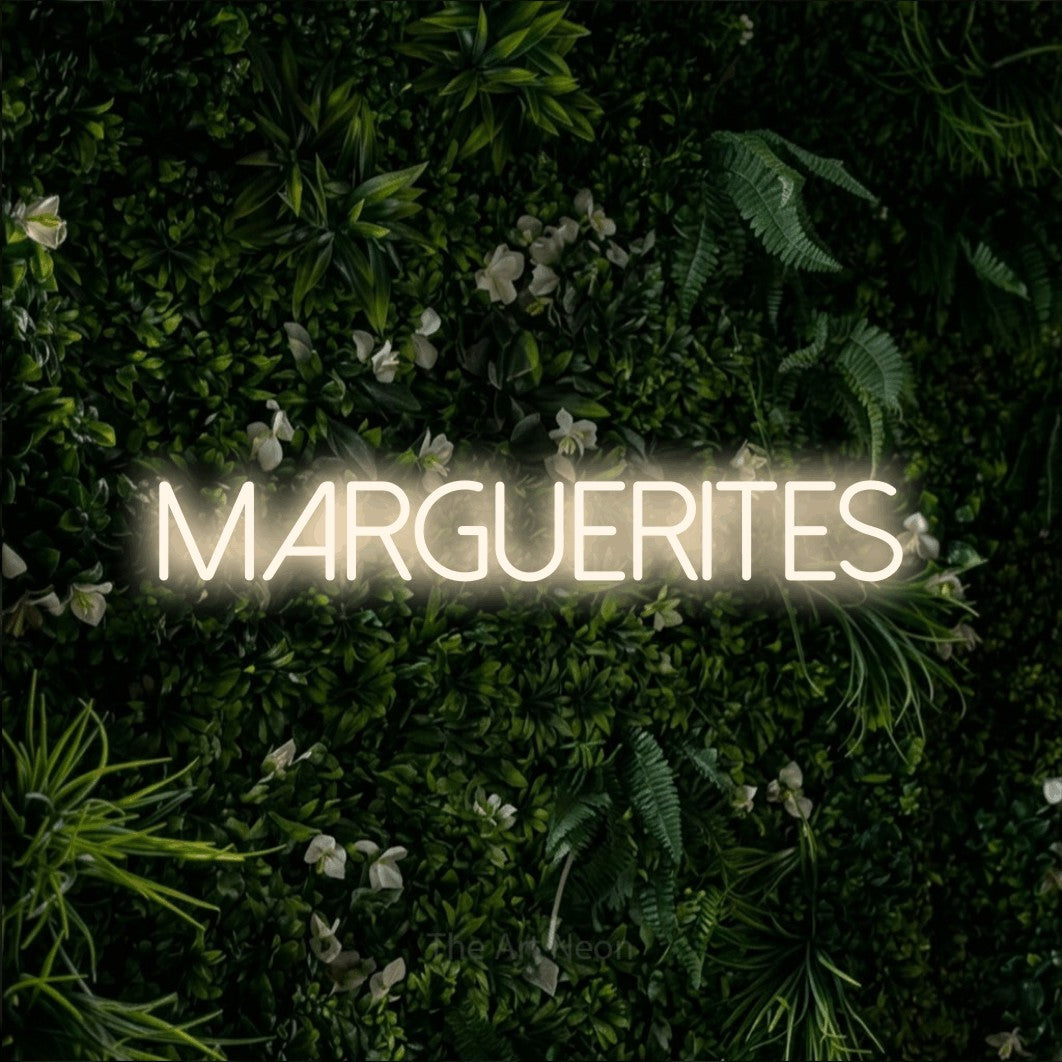 “Marguerites” LED neon sign in warm white, with thin sans-serif lettering, shown against a dense green plant wall.