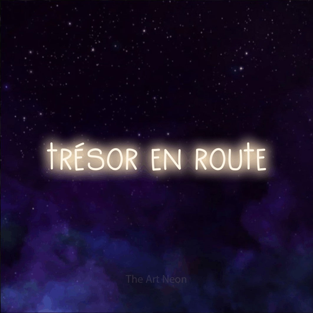 “Trésor en route” LED neon sign in warm white, with narrow hand-drawn lettering, shown against a purple galaxy backdrop.