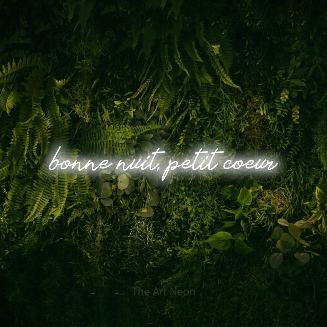 “Bonne nuit, petit cœur” LED neon sign in cool white, with cursive lettering, shown against a dark moss and forest backdrop.