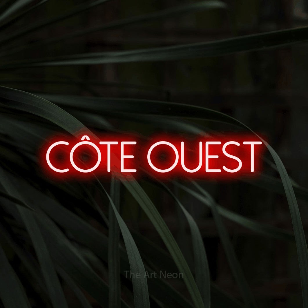 Néon LED « Côte ouest » en rouge, en lettres fines sans empattement, mis en scène sur un feuillage sombre en gros plan, pour un décor canadien.