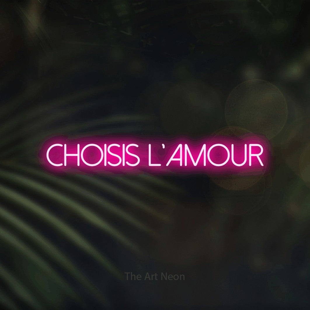 “Choisis l'amour” LED neon sign in hot pink, with thin sans-serif lettering, shown against a blurred palm and bokeh-light backdrop.