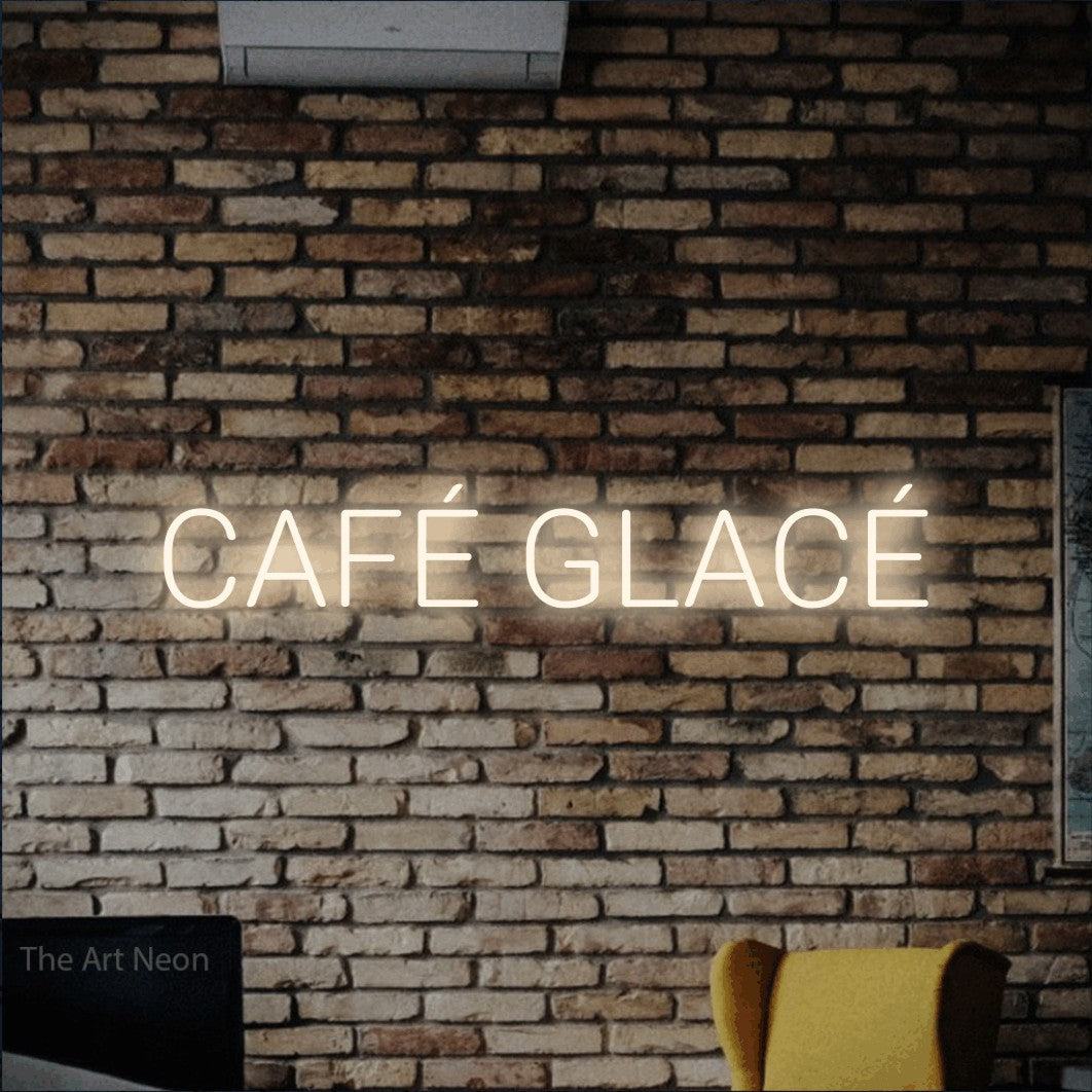 “Café glacé” LED neon sign in warm white, with rounded sans-serif lettering, shown against warm-toned brickwork.