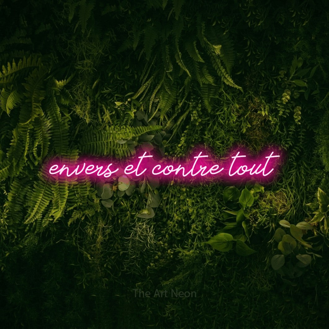“Envers et contre tout” LED neon sign in hot pink, with cursive lettering, shown against a dark moss and forest backdrop.