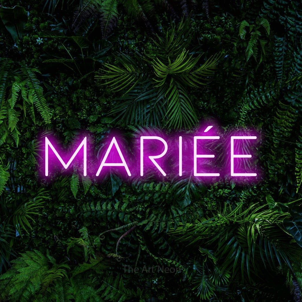 “Mariée” LED neon sign in pink, with thin, widely spaced lettering, shown against dense tropical foliage.