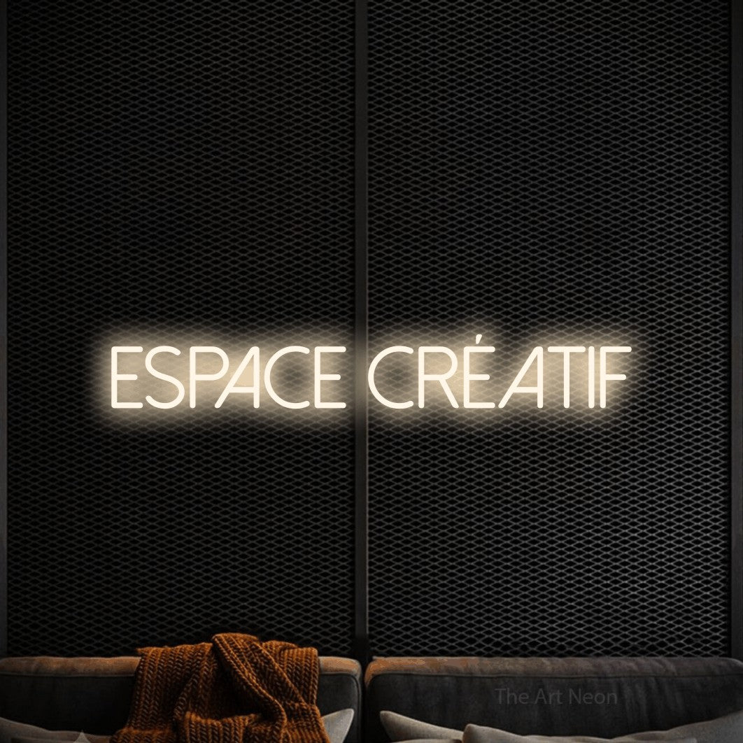Composition en néon LED « Espace créatif » en blanc chaud, en lettres fines sans empattement, mise en valeur dans un coin salon moderne aux tons noirs, pour un bureau ou une entreprise.