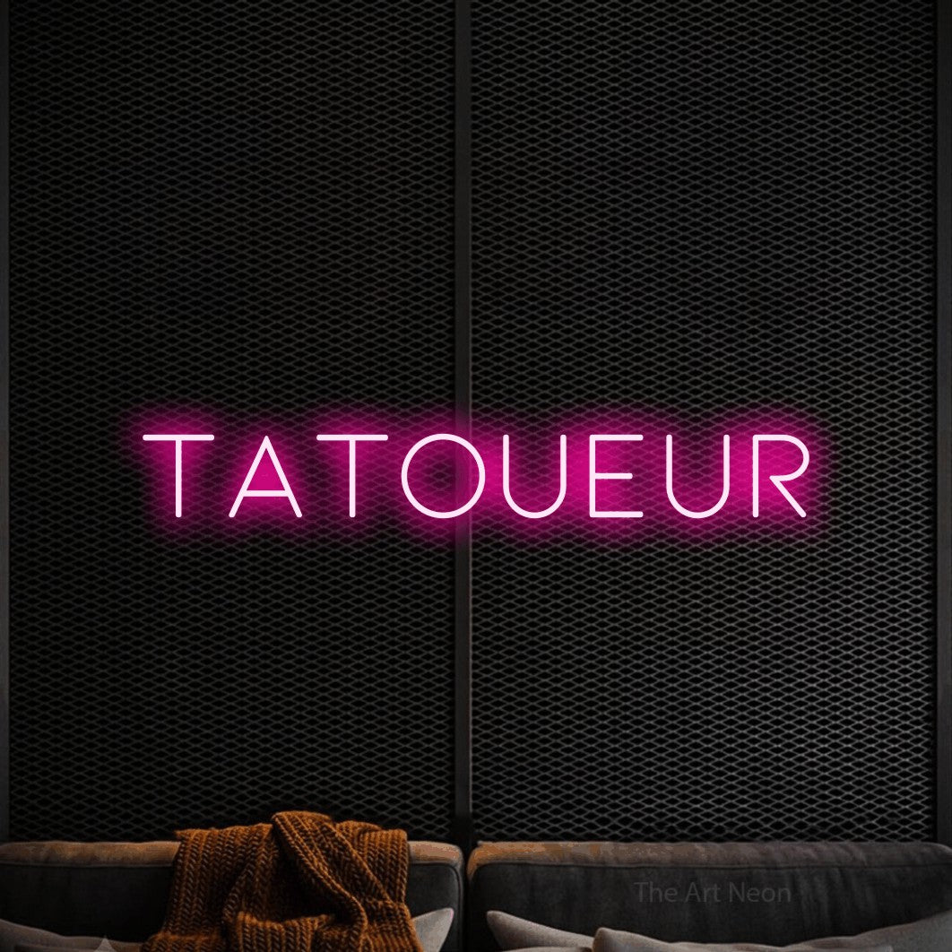 “Tatoueur” LED neon sign in hot pink, with thin, widely spaced lettering, shown against a modern dark-toned seating area.