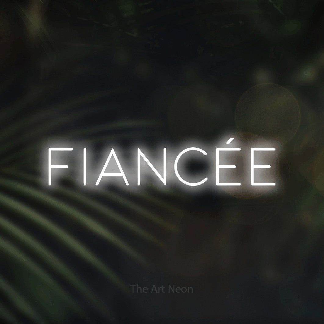 “Fiancée” LED neon sign in cool white, with thin, widely spaced lettering, shown against a blurred palm and bokeh-light backdrop.