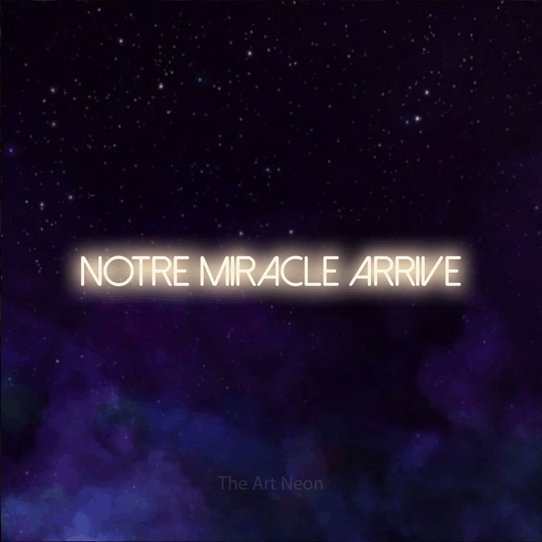 “Notre miracle arrive” LED neon sign in warm white, with thin sans-serif lettering, shown against a purple galaxy backdrop.