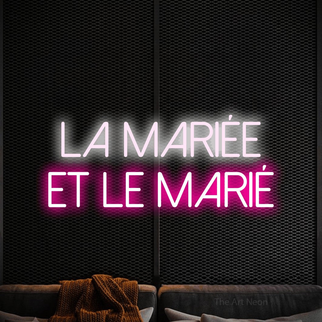 “La mariée et le marié” LED neon sign in cool white on the upper line and hot pink on the lower line, with thin sans-serif lettering across 2 lines, shown against a modern dark-toned seating area.