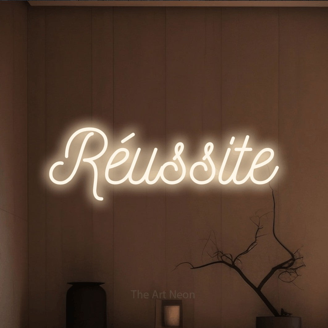 “Réussite” LED neon sign in warm white, with ornate cursive lettering, shown against a simple earth-toned interior.