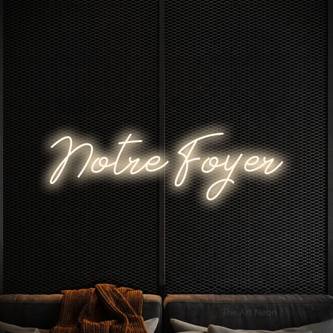“Notre foyer” LED neon sign in warm white, with cursive lettering, shown against a modern dark-toned seating area.