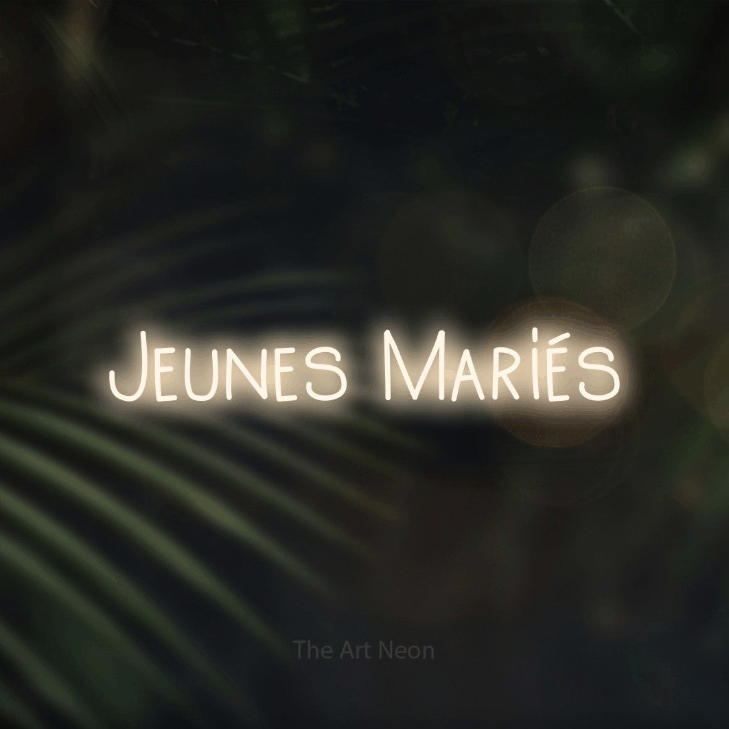 Composition en néon LED « Jeunes mariés » en blanc chaud, en lettres étroites dessinées à la main, mise en valeur sur un fond flou de palmiers et de lumières bokeh, pour une réception de mariage.