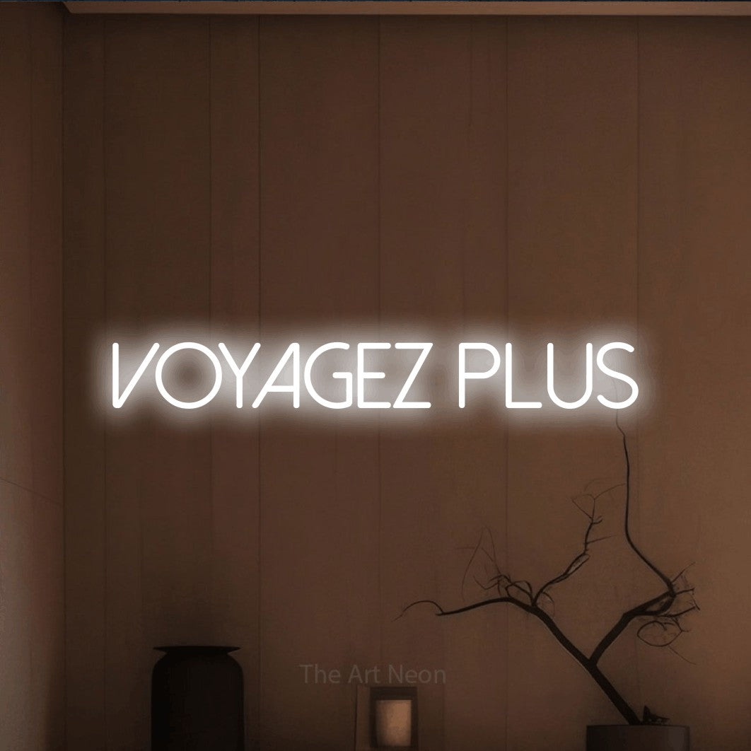 “Voyagez plus” LED neon sign in cool white, with thin sans-serif lettering, shown against a simple earth-toned interior.